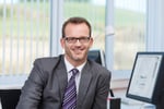 Friendly businessman wearing glasses sitting at his desk in the office looking at the camera with a smile